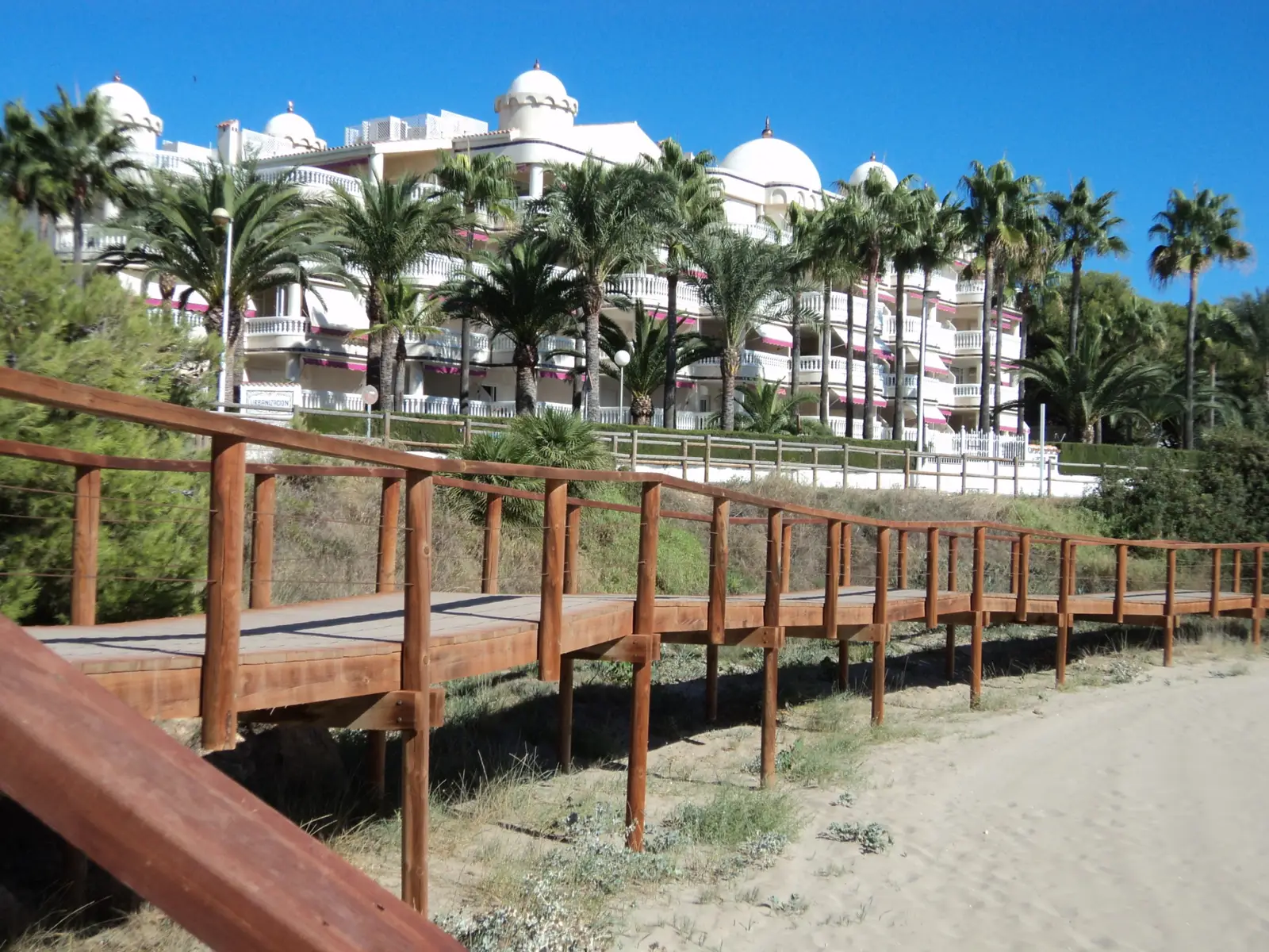 Bâtiment blanc à coupoles de la résidence Casablanca vu depuis la passerelle en bois de la plage Romana