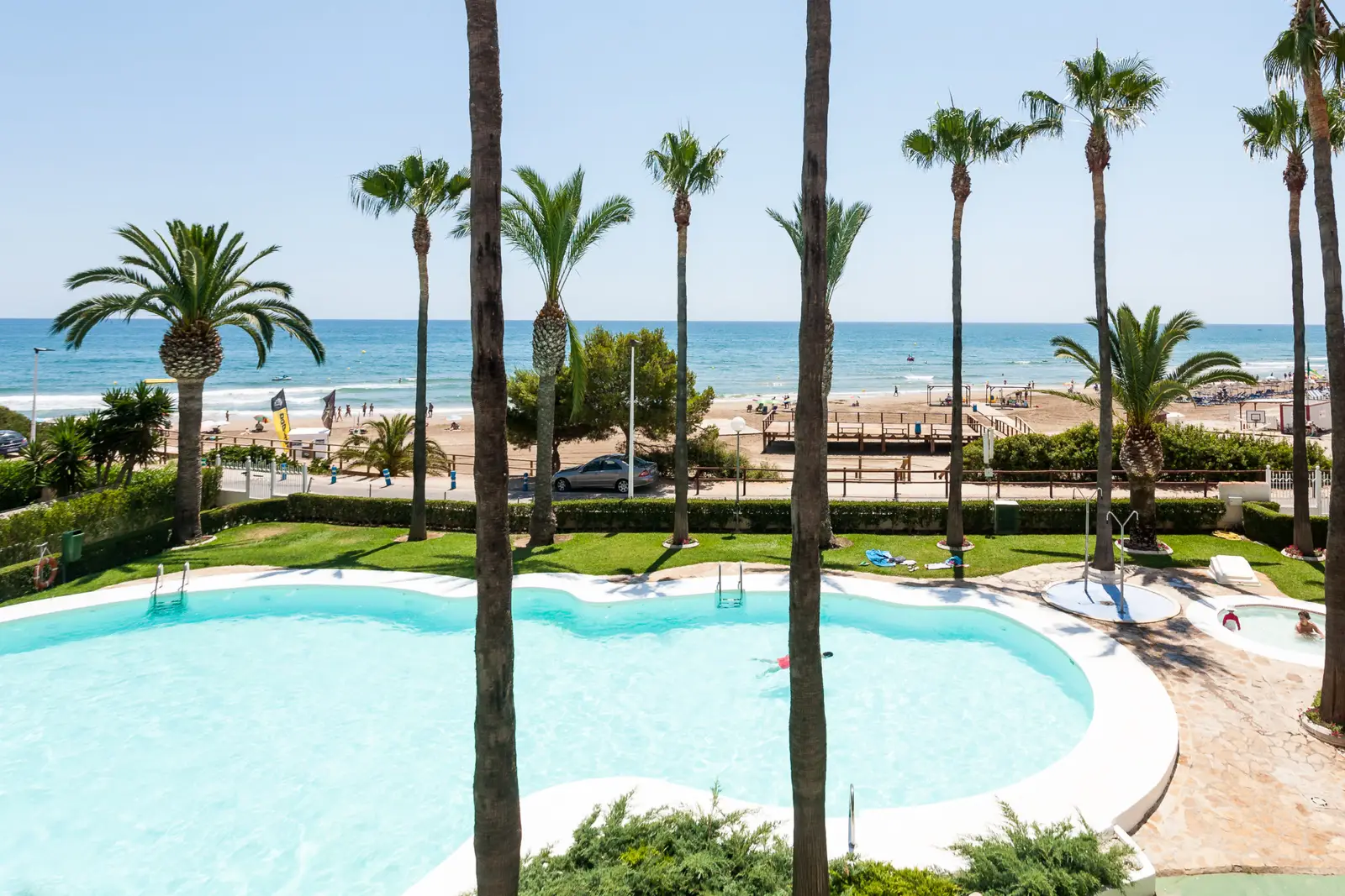 Piscine et palmiers de la résidence Casablanca avec la plage Romana d'Alcossebre et la mer au fond